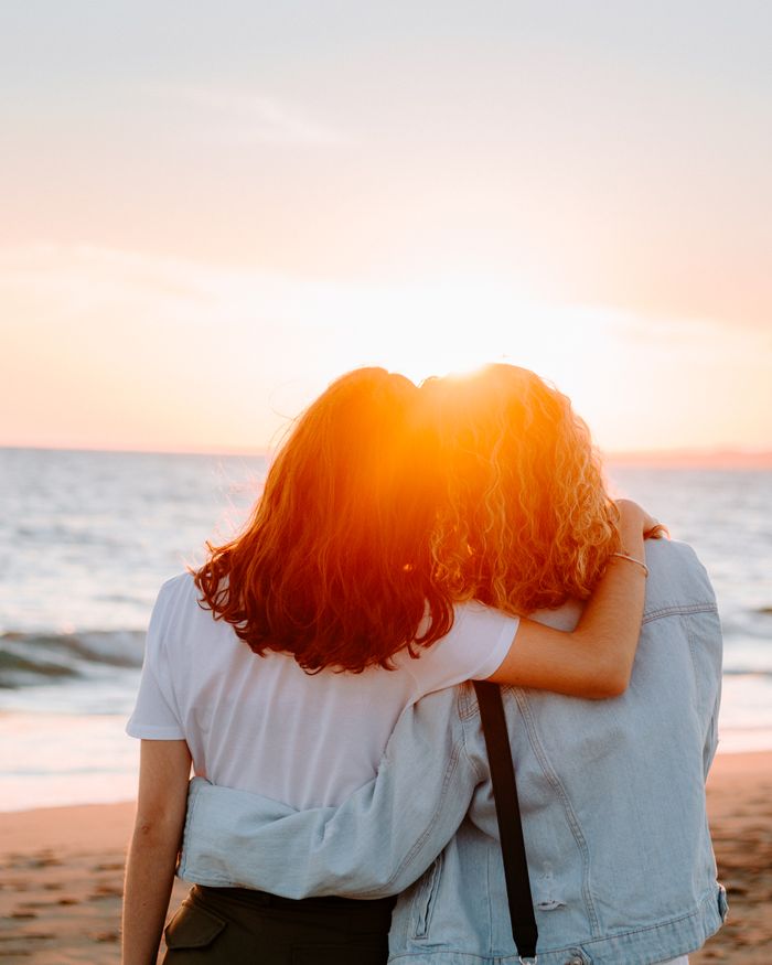 pexels photo 14252345 Two women hug by the sea at sunset, enjoying a serene seaside moment.