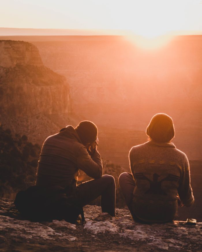 Two people sit on a canyon edge, enjoying a warm sunset horizon.