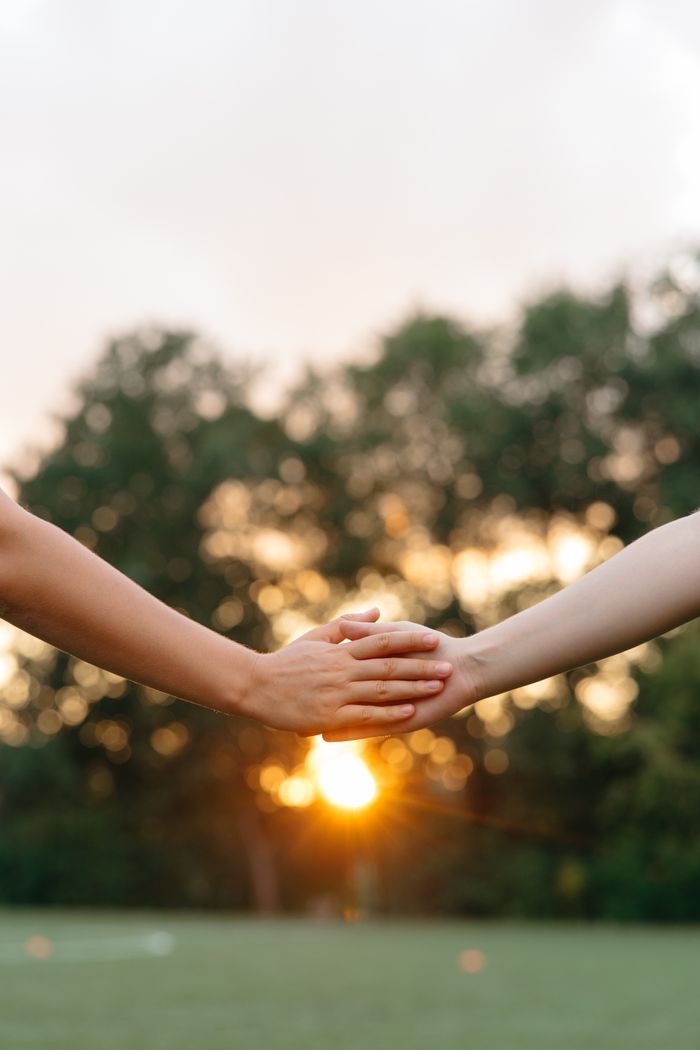 Two people holding hands at sunset, a symbol of connection and unity.